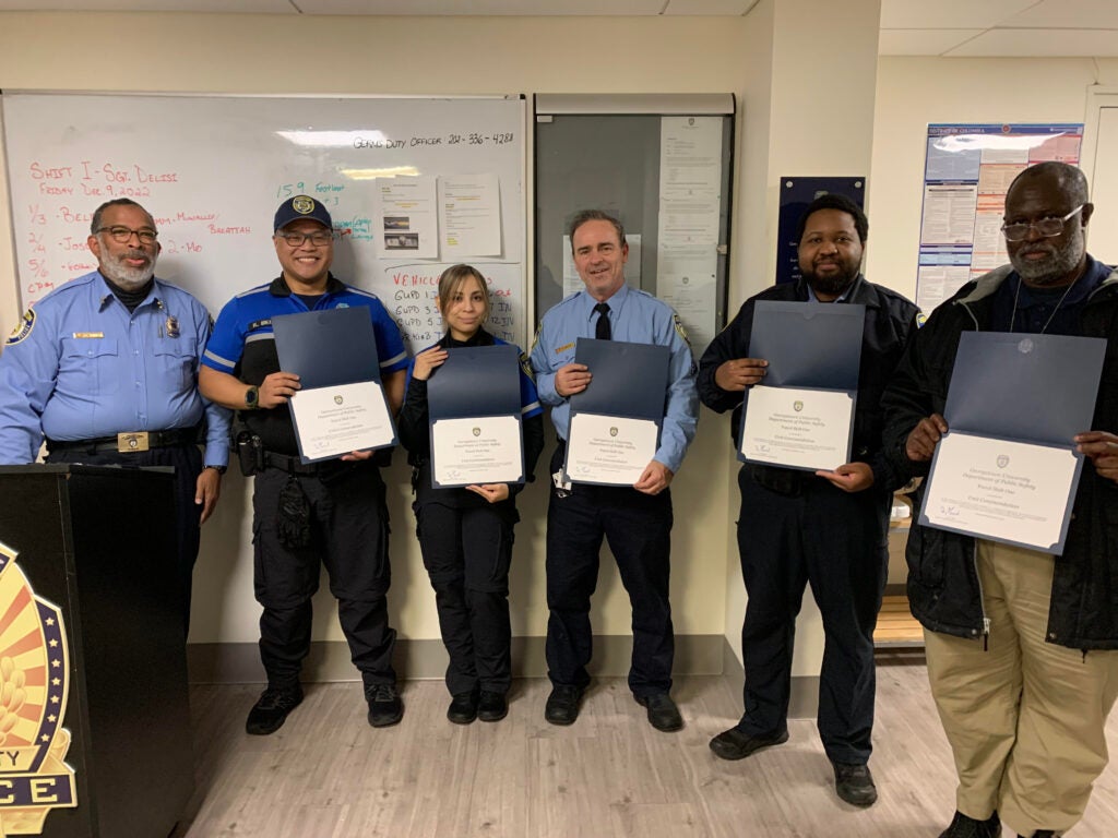 Six members of the GUPD stand smiling, five are holding certificates.